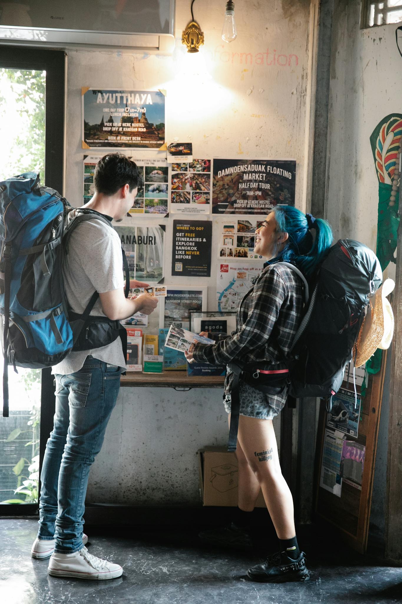 Two backpackers examining maps and brochures inside a travel information center.